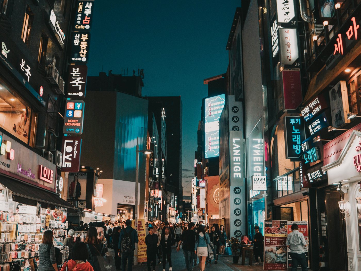 명동 저녁 상권 거리 — 뷰티 브랜드 네온과 외국인 관광객으로 붐비는 쇼핑 거리